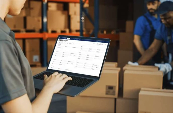 Warehouse employee reviewing inventory data on a laptop while comparing WMS vs ERP systems.