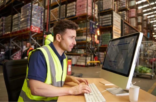 Warehouse employee using a desktop system to manage operations in a WMS vs ERP environment.