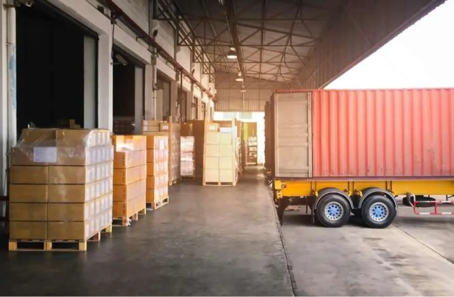 Warehouse loading dock with pallets and a container trailer, representing types of WMS used in logistics operations.