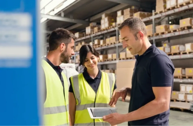 Warehouse supervisor providing WMS training to employees using a tablet.