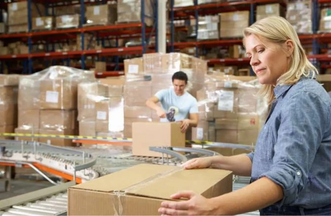 Warehouse employees packing orders on a conveyor, illustrating the benefits of WMS for faster fulfillment.